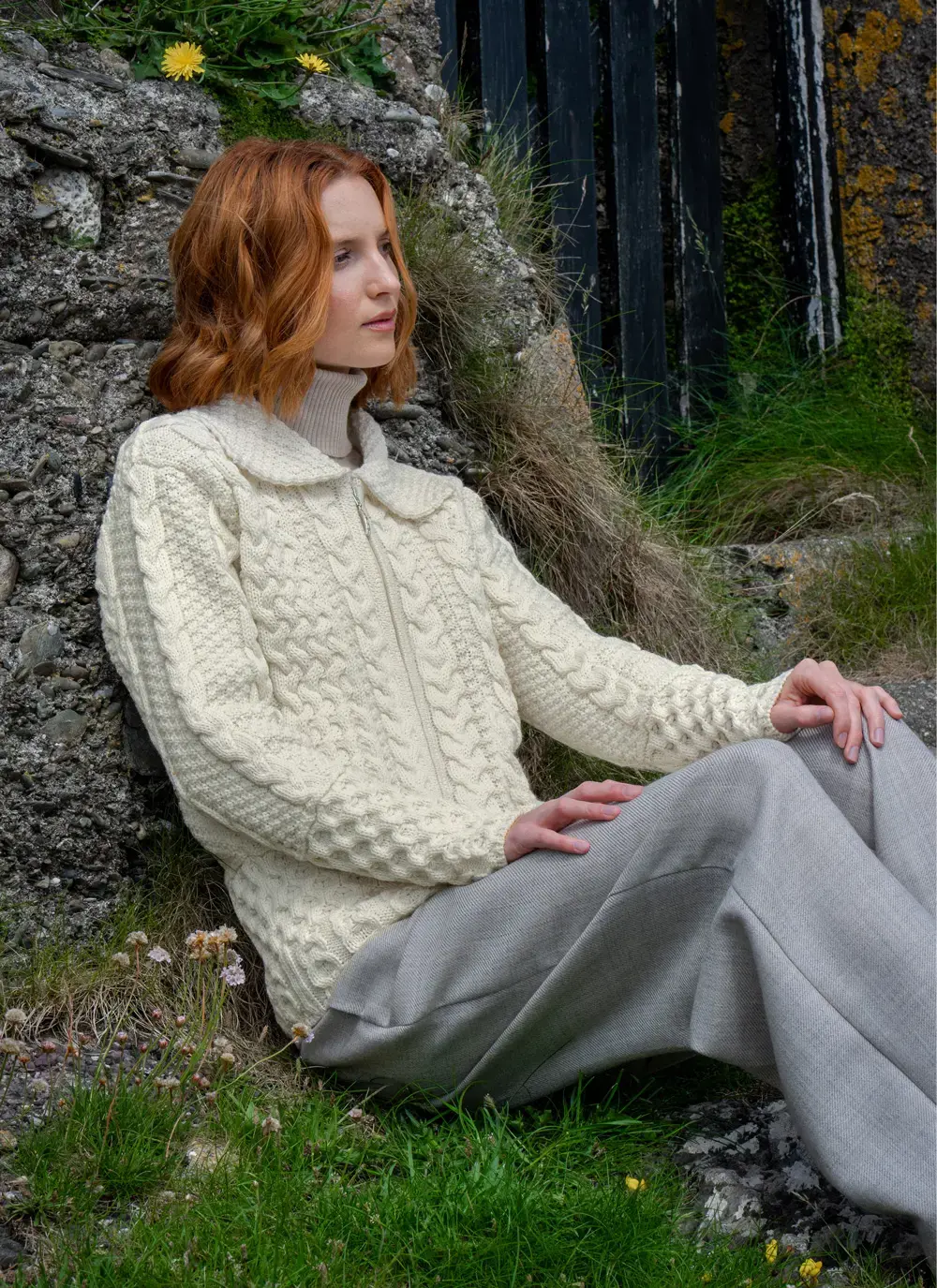 Red haired model sitting in Grace Full Zip Aran Cardigan in Natural